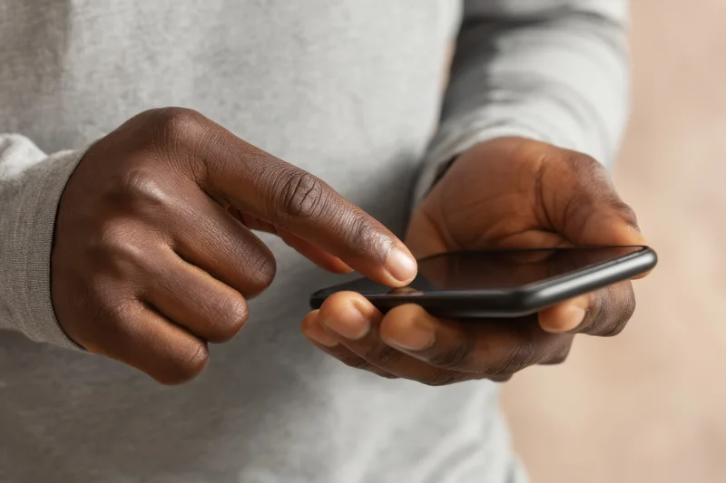 Close-up of hands tapping a smartphone while holding it in a gray sweater