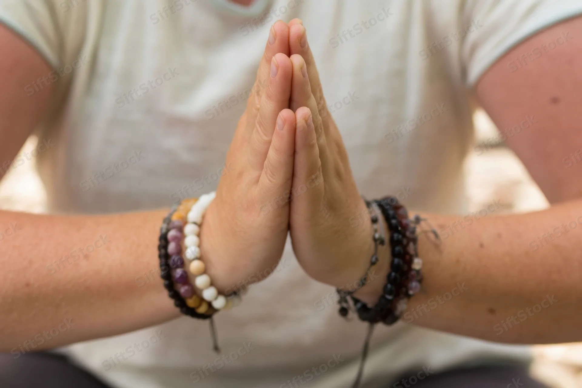 Woman's hands pressed together in prayer pose with beaded bracelets, outdoors in natural light
