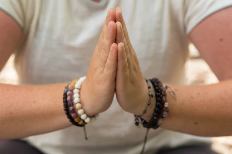Woman's hands pressed together in prayer pose with beaded bracelets, outdoors in natural light