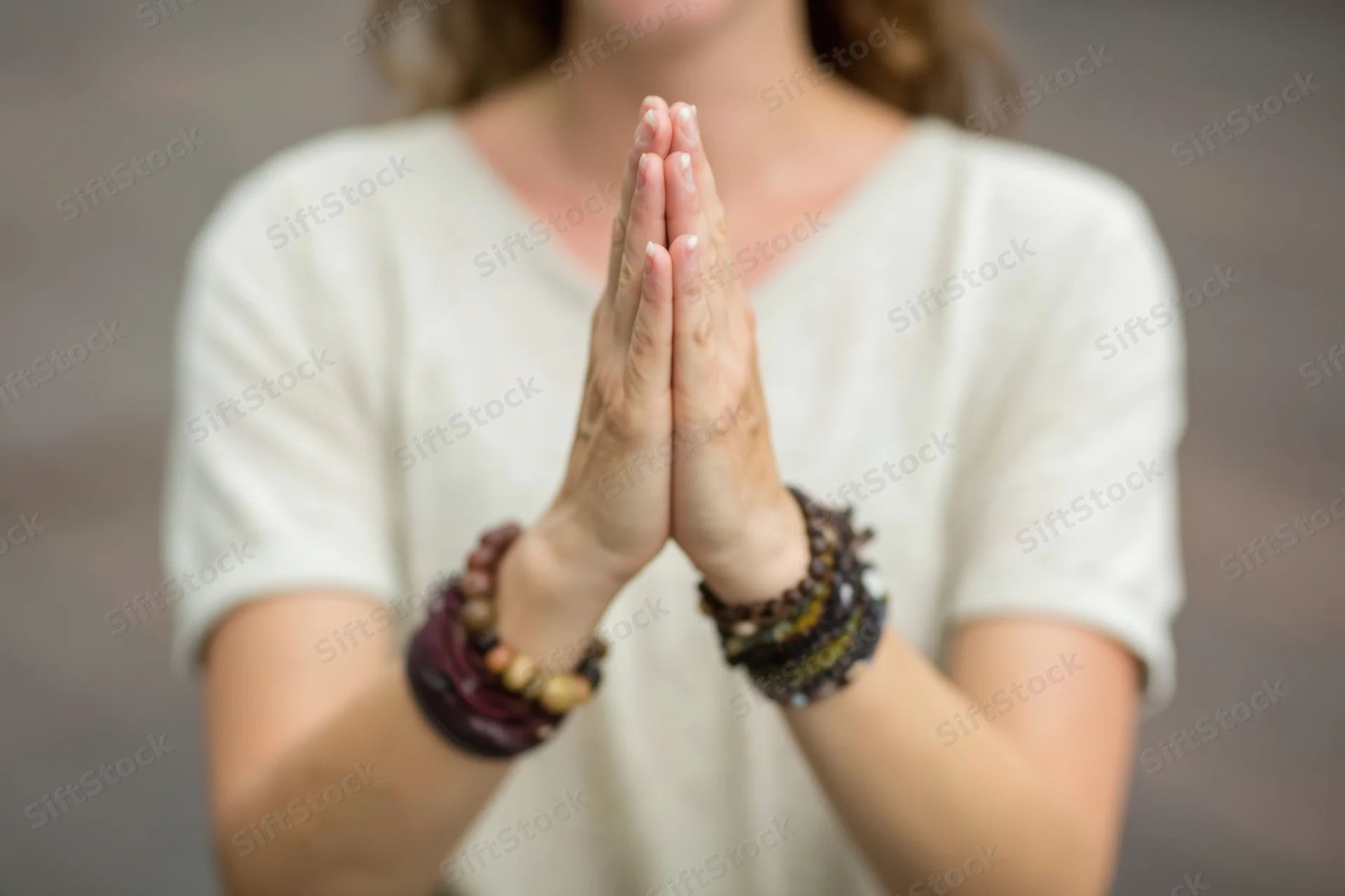 Woman with hands pressed together in prayer pose wearing beaded bracelets and white shirt