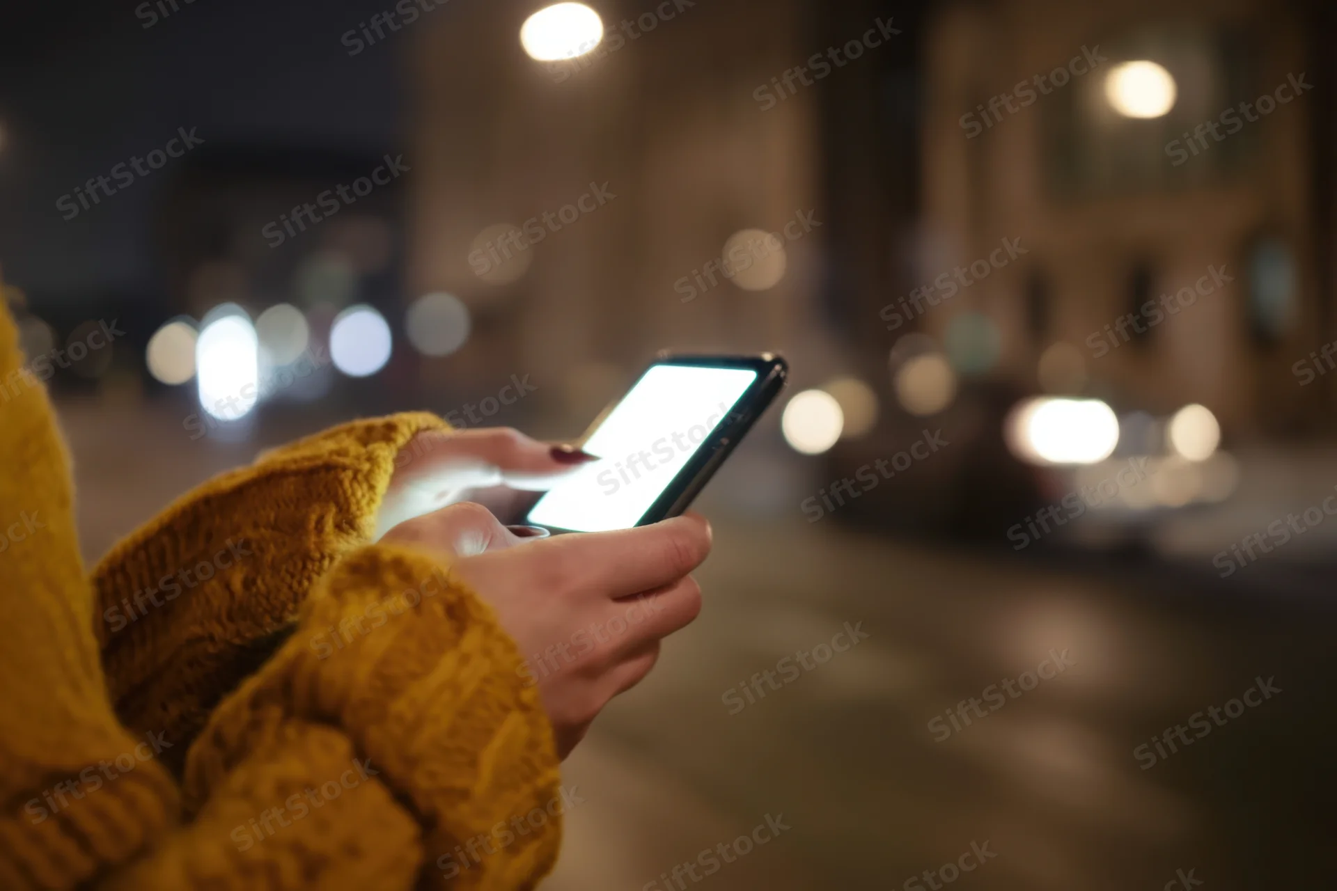 Woman’s hands holding smartphone with glowing screen on city street at night
