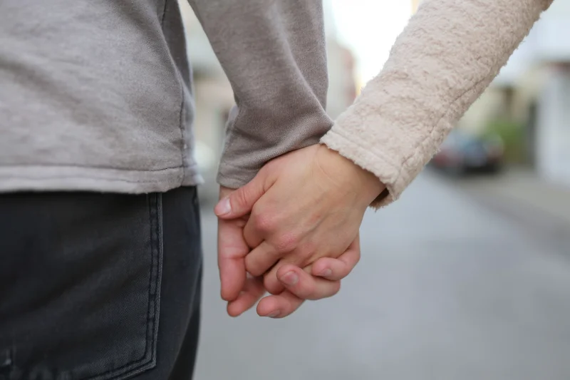 Two people holding hands while walking on a city sidewalk