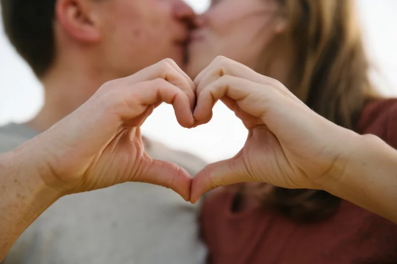 Couple kissing with hands forming heart shape in soft focus outdoor setting