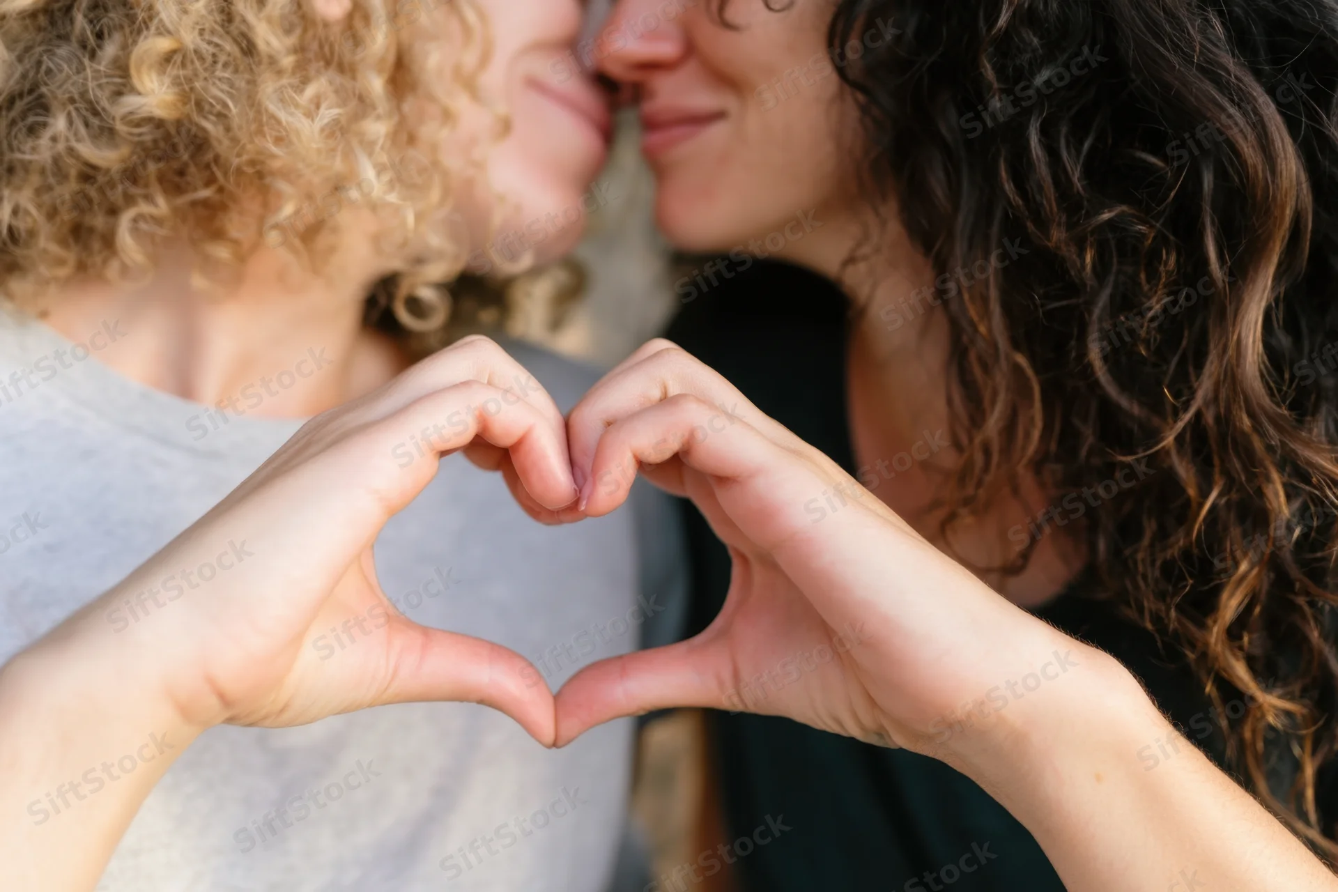 Two women forming a heart shape with their hands while facing each other closely