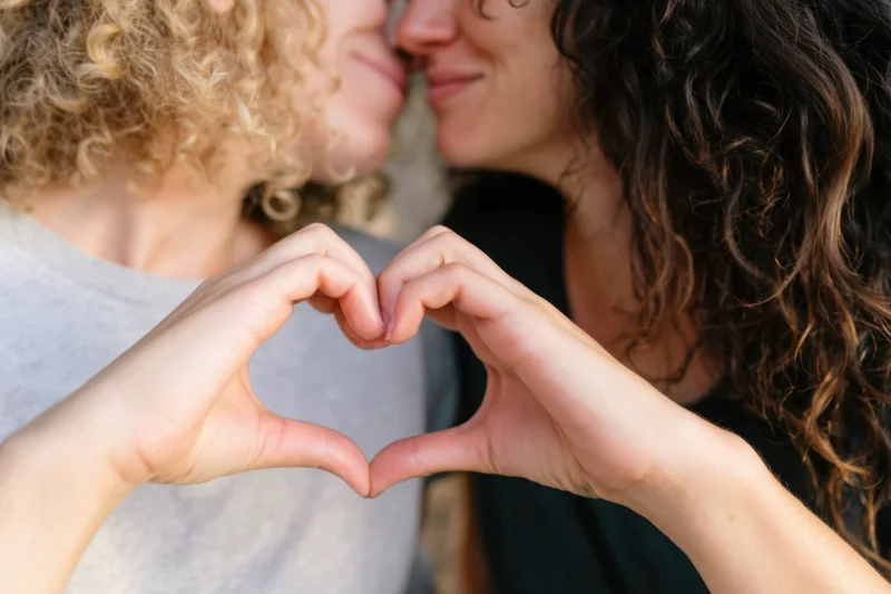 Two women forming a heart shape with their hands while facing each other closely