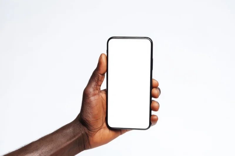 Dark-skinned hand holding a black-framed smartphone with blank white screen against white background