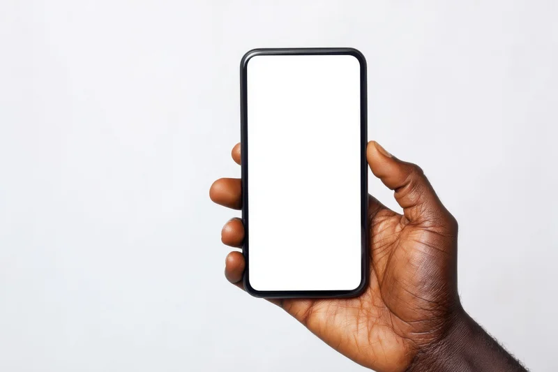 Dark-skinned hand holding a black-framed smartphone with blank white screen against white background
