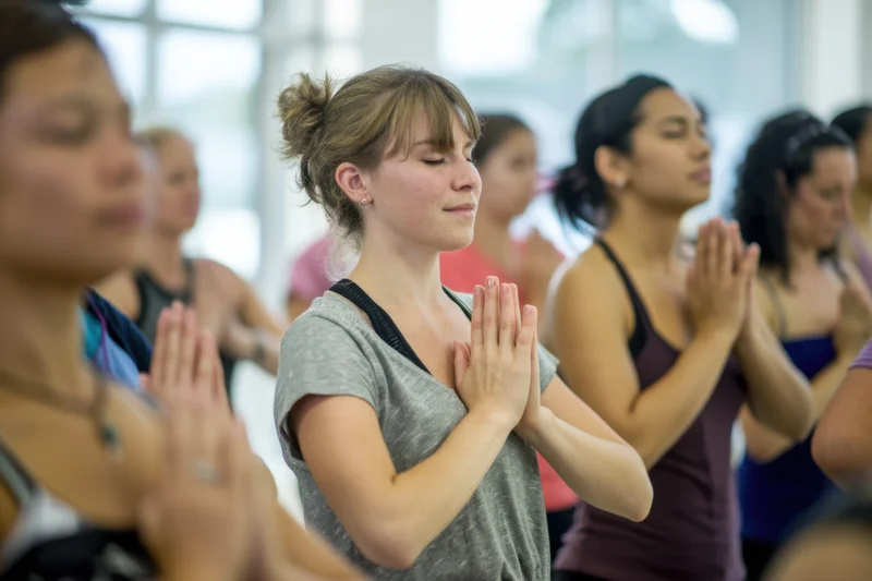 Women practicing yoga with hands in prayer pose in a sunlit studio