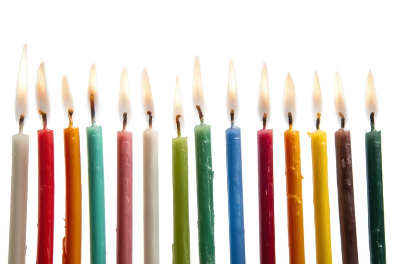 Row of tall colorful lit candles against white background