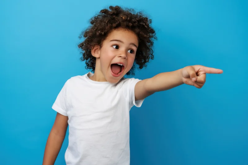 Young child pointing excitedly with open mouth against blue background