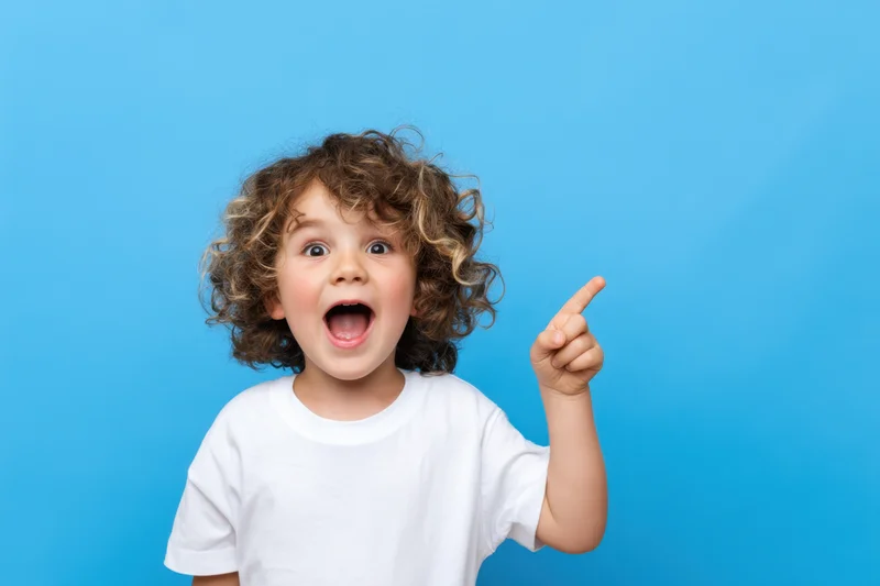 Young child with curly hair pointing upward in excitement against a blue background