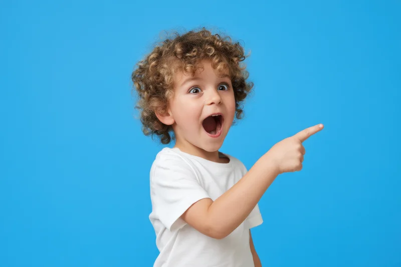 Young boy with curly hair pointing excitedly against blue background