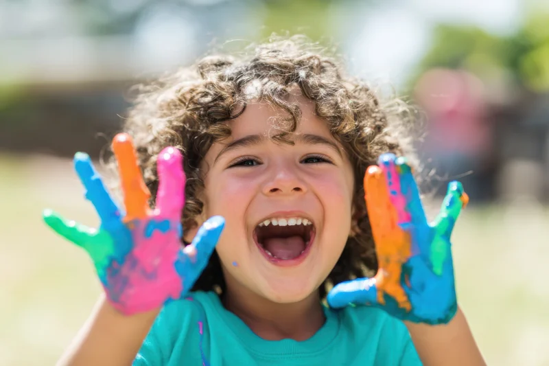 Child laughing with paint-covered hands outdoors