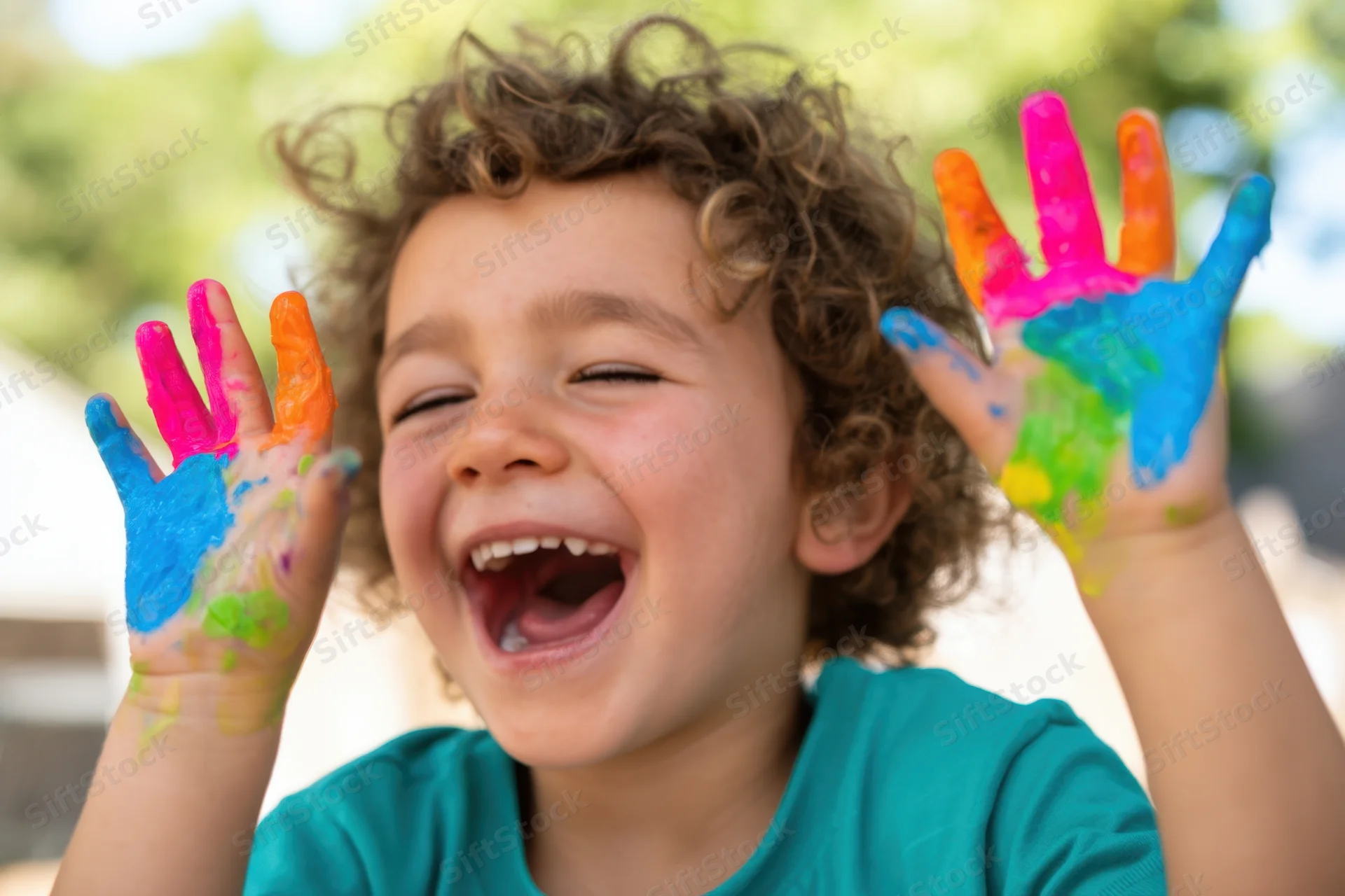 Child laughing with paint-covered hands raised outdoors