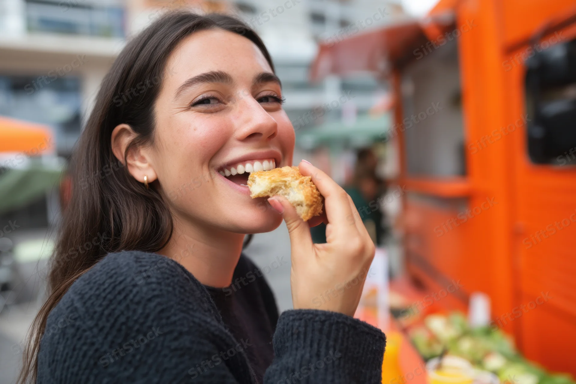 Young woman smiling while eating a pastry outdoors near a food truck