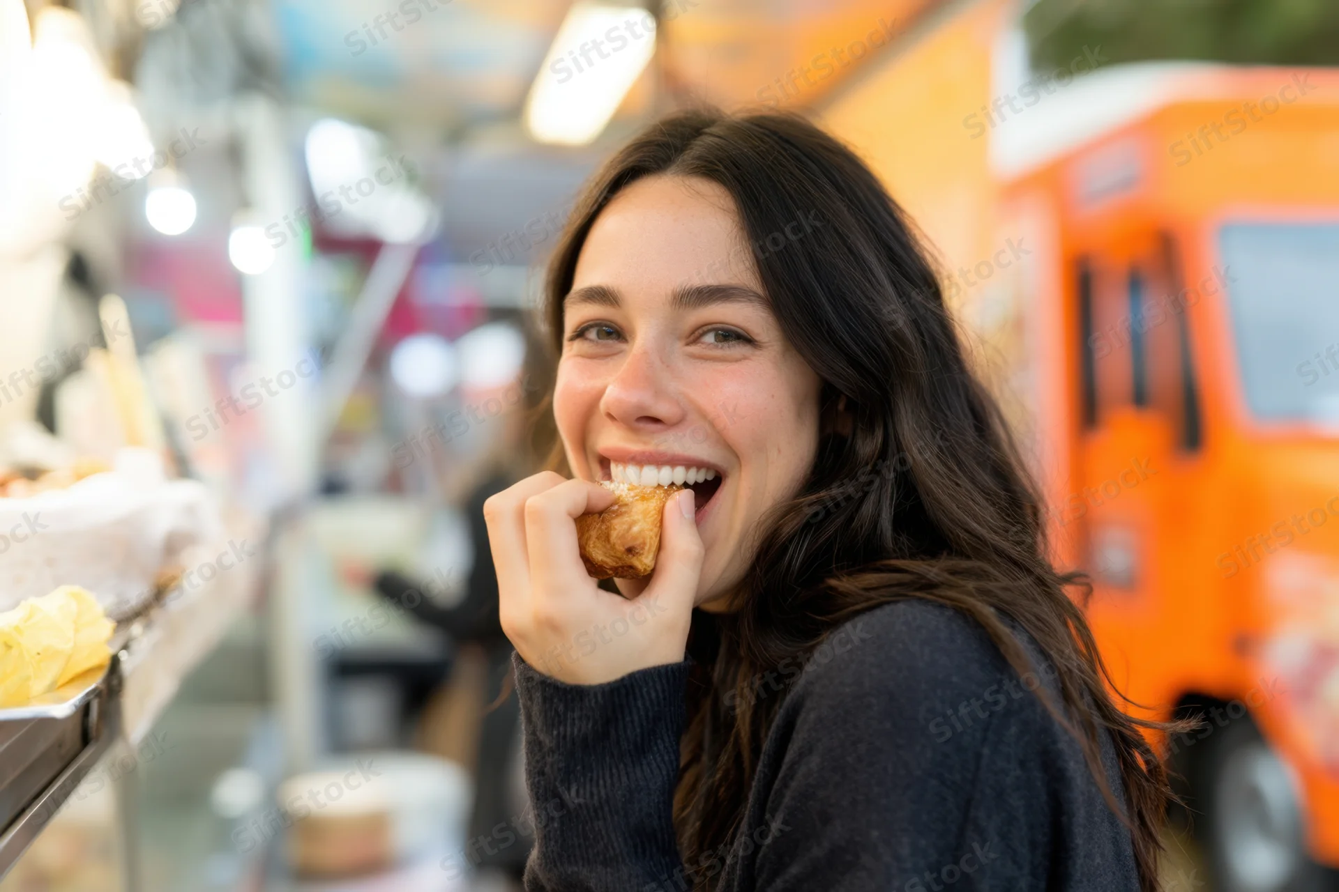 Woman eating a snack at a street food market, smiling at the camera