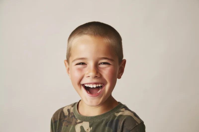 Young boy laughing with wide smile wearing camouflage tshirt in studio setting