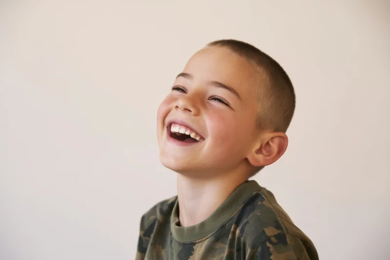 Young boy laughing with wide smile, wearing camouflage tshirt, against plain white background