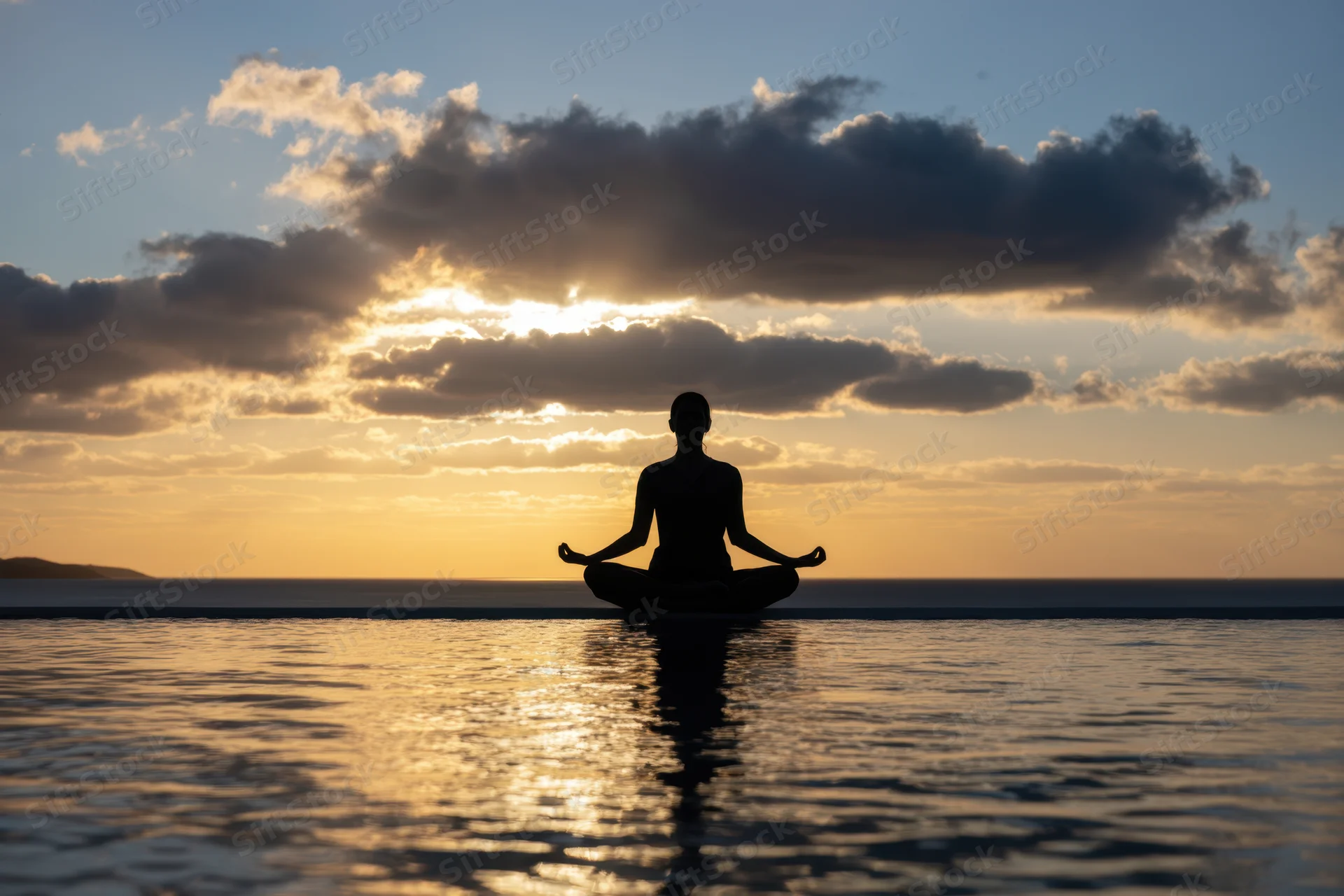 Woman meditating in lotus pose at sunset by the ocean