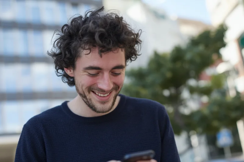 Young man smiling while using smartphone outdoors on city street