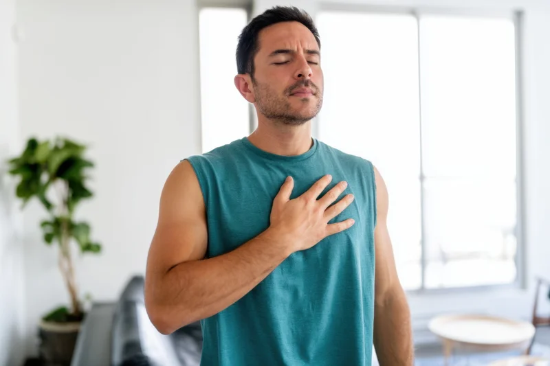Man holding chest in discomfort indoors near window