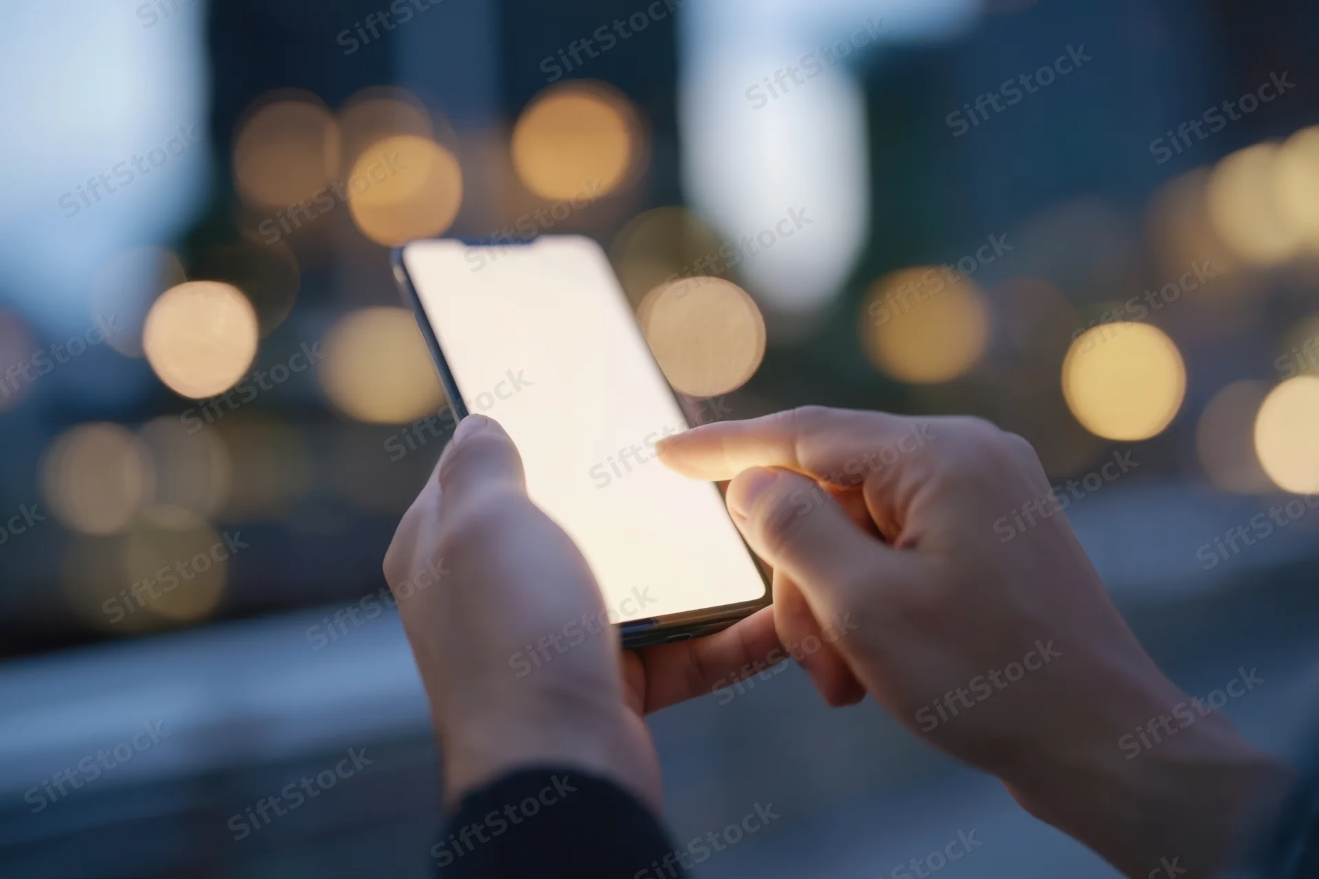 Hands holding smartphone with glowing screen in urban outdoor setting at night