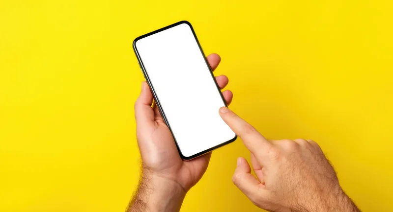 Hands holding smartphone with blank white screen against yellow background, finger pointing at display