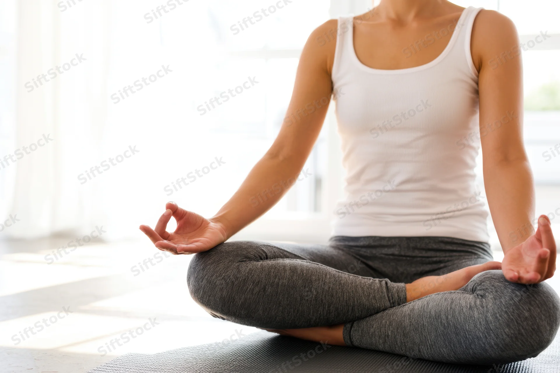 Woman meditating cross-legged on a yoga mat in a sunlit room