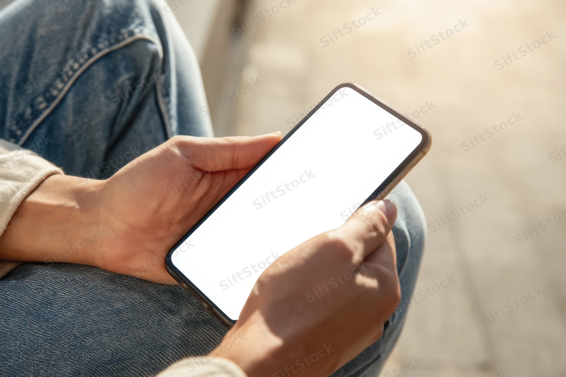 Woman holding smartphone with blank white screen outdoors while sitting on steps