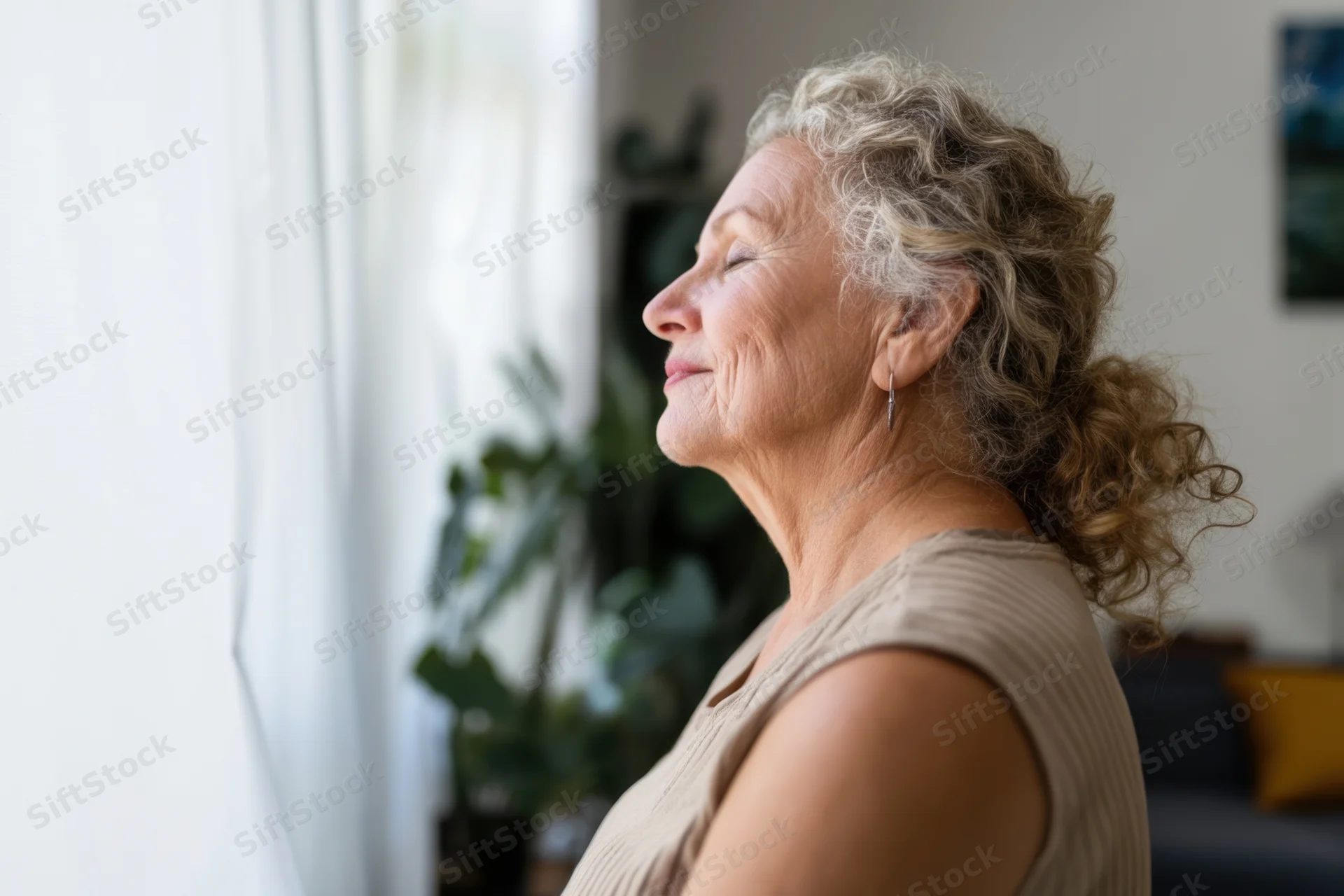 Senior woman in profile with eyes closed breathing calmly by a window in a living room
