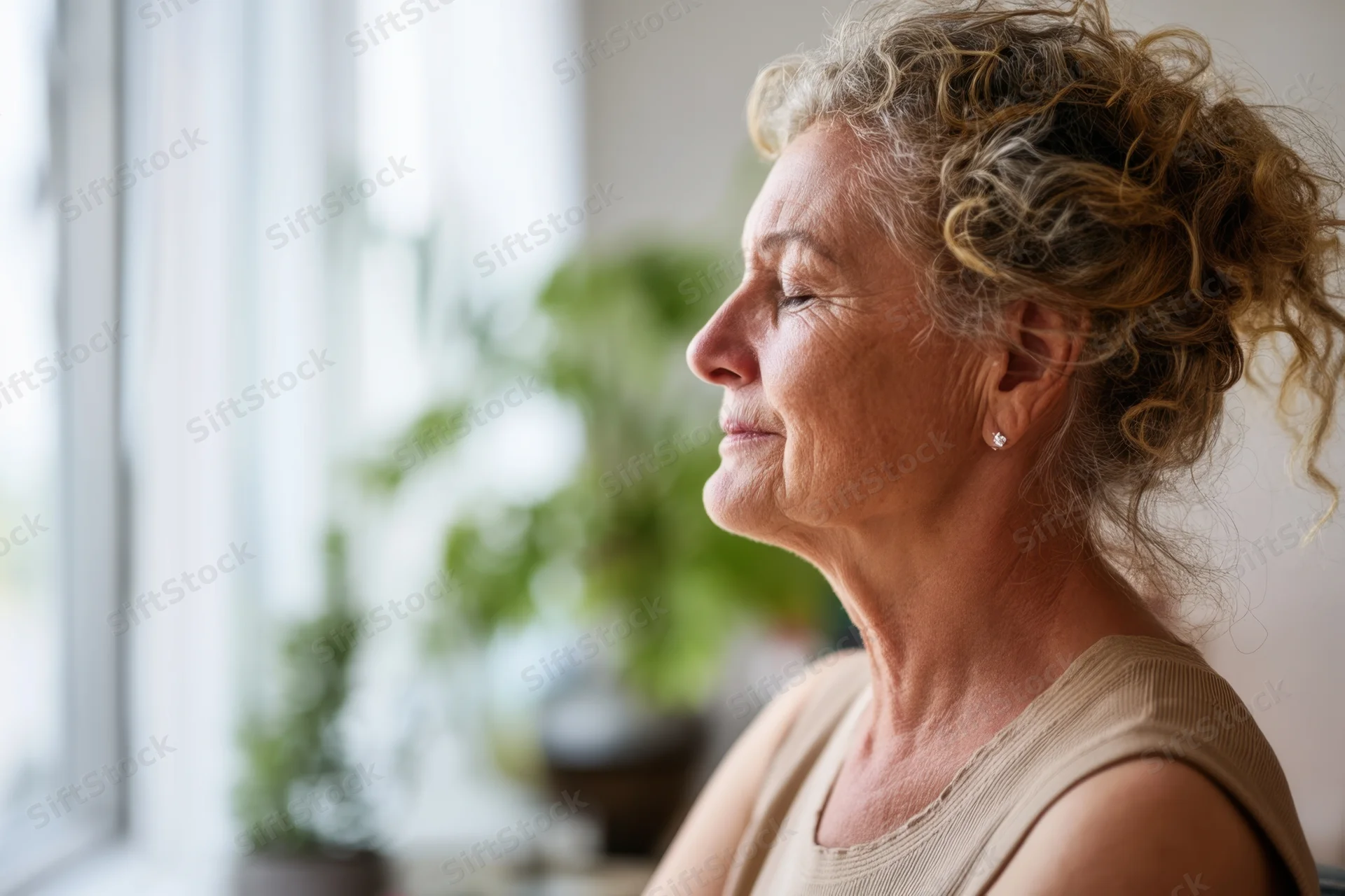 Senior woman in profile with eyes closed sitting by window in home