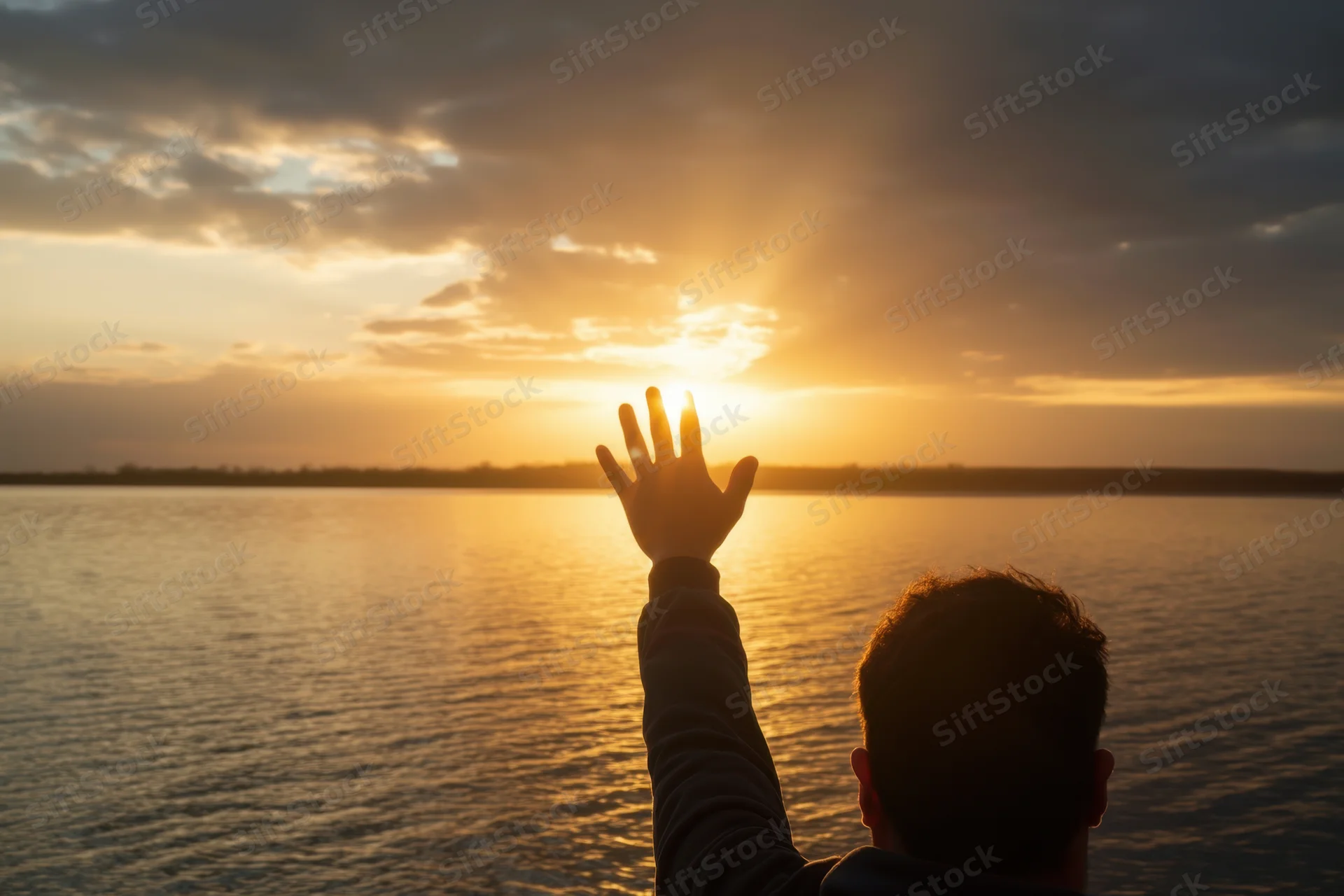 Man reaching hand toward sunset over lake