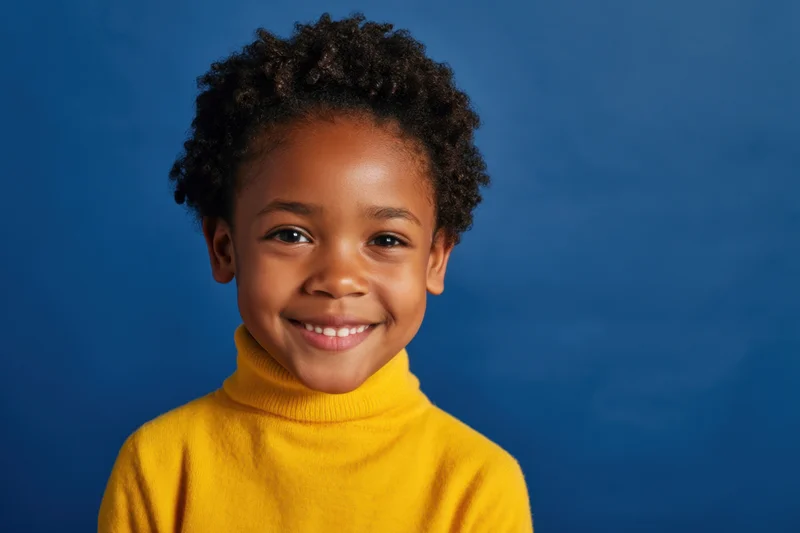 Smiling young african girl in yellow turtleneck sweater against blue background