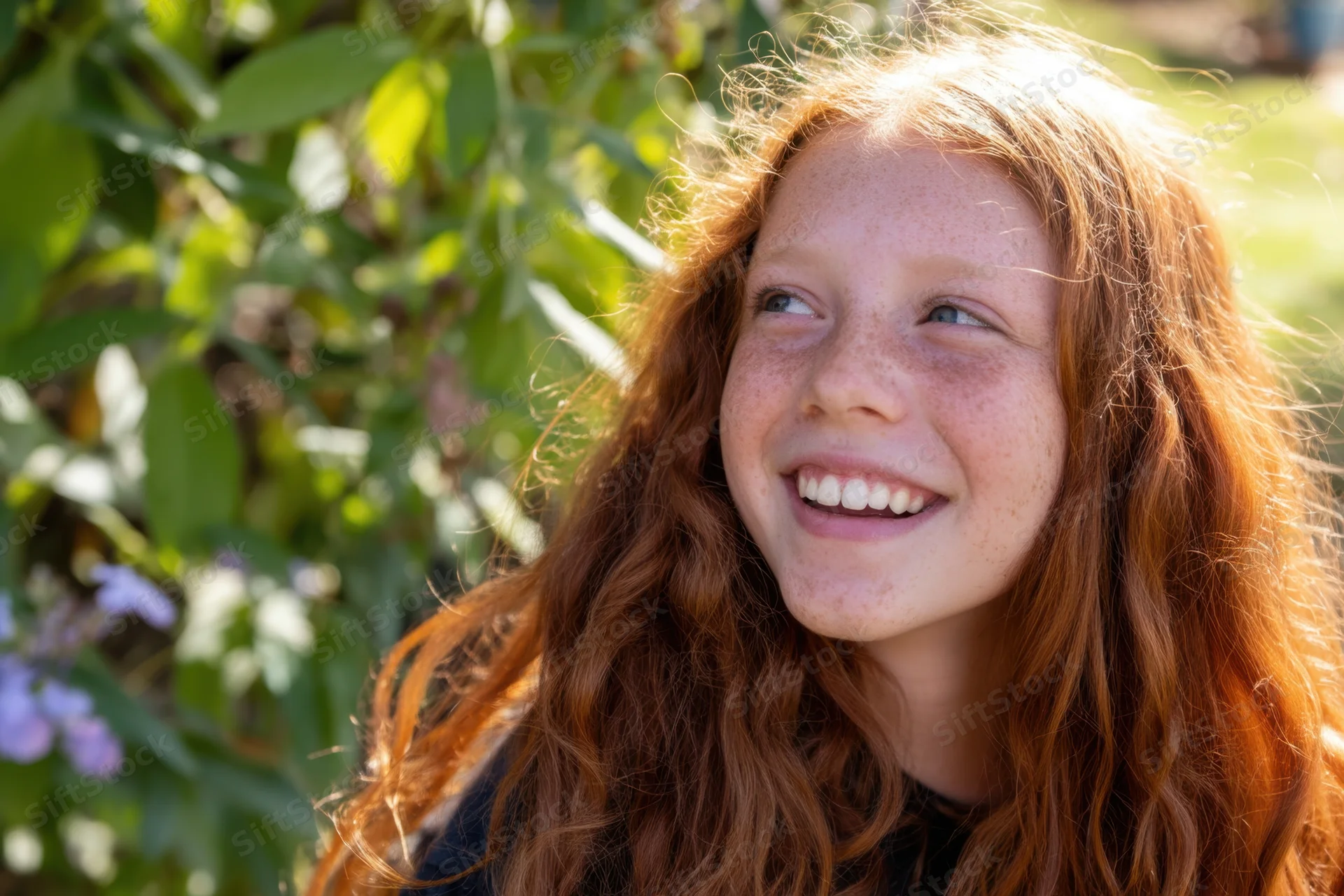 Smiling red-haired girl with freckles looking up in a sunlit garden