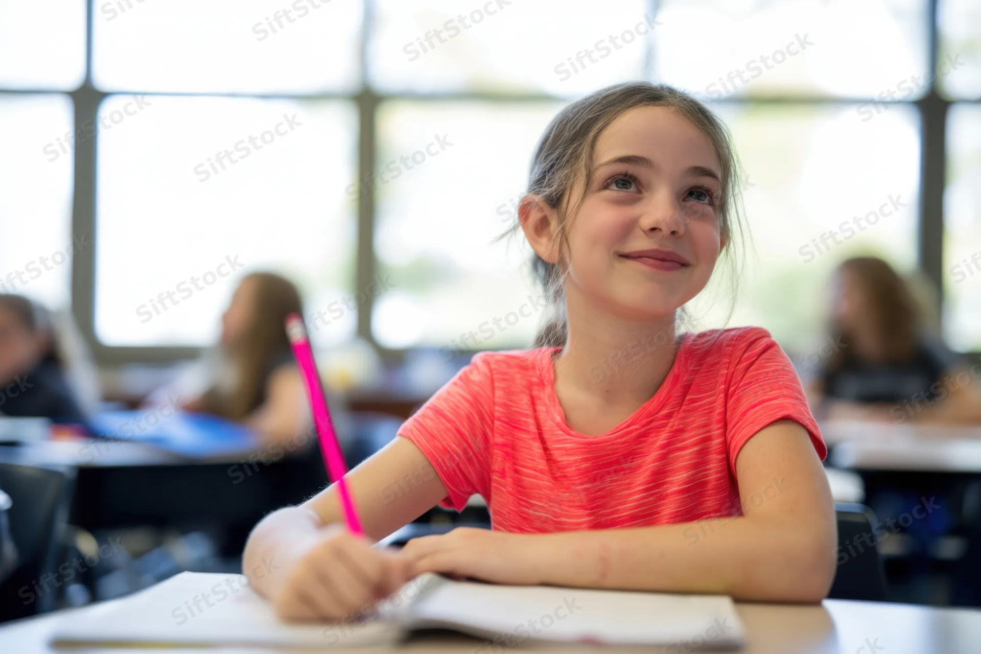 Young girl smiling while writing in a notebook at a classroom desk