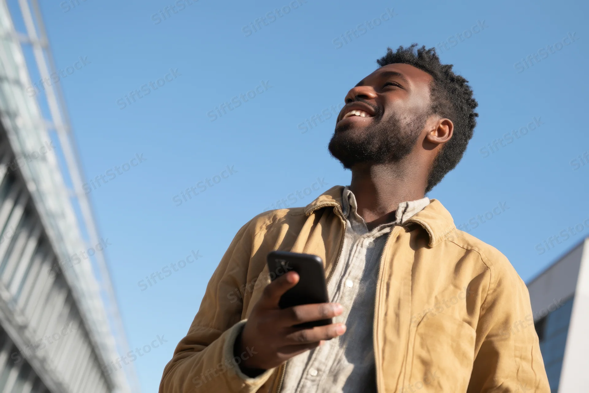 Young black man smiling while holding smartphone outdoors in urban setting