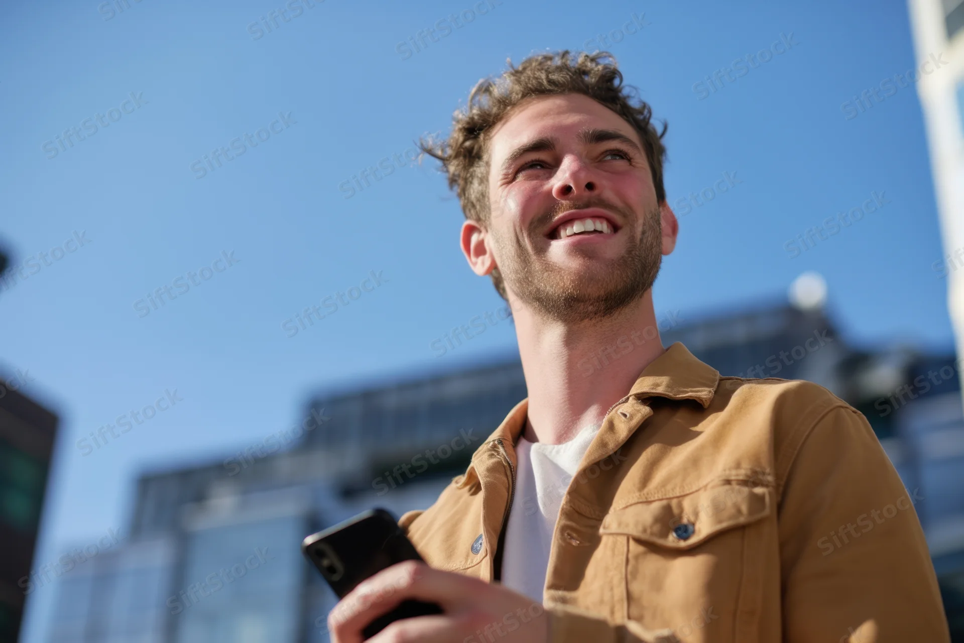 Young man smiling while holding smartphone outdoors in urban setting
