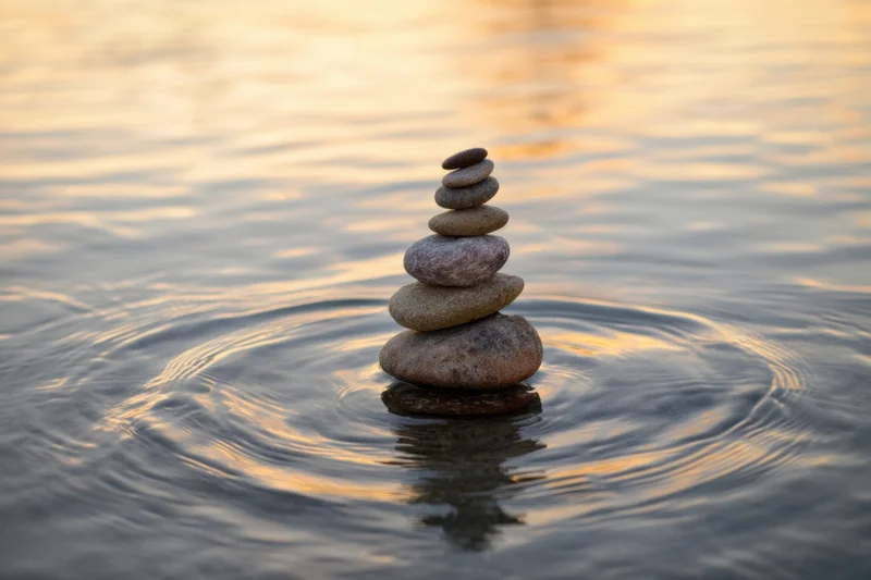 Balanced stone stack rising from rippling water at sunset