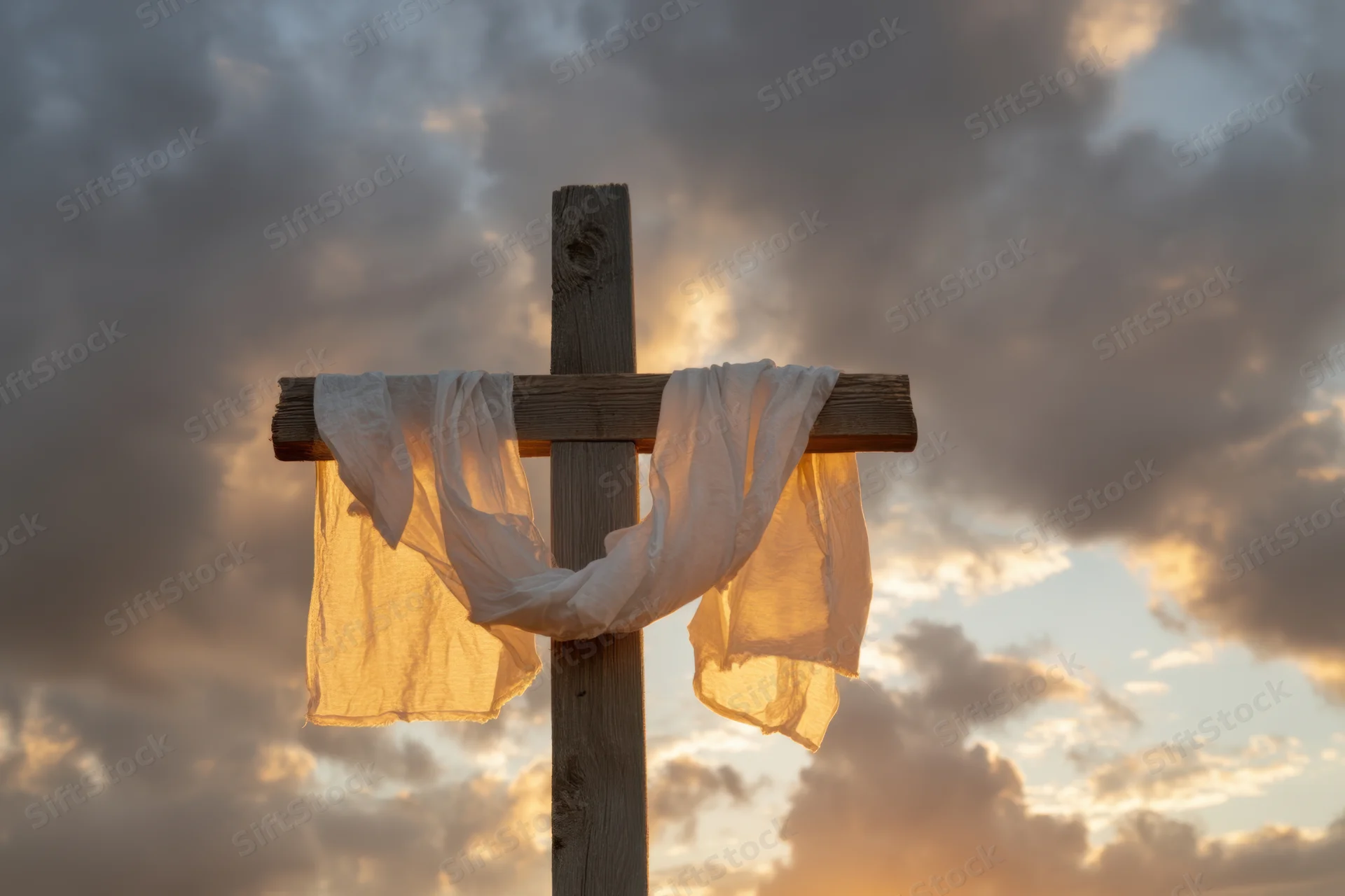Weathered wooden cross with white cloth draped over it against dramatic sunset sky