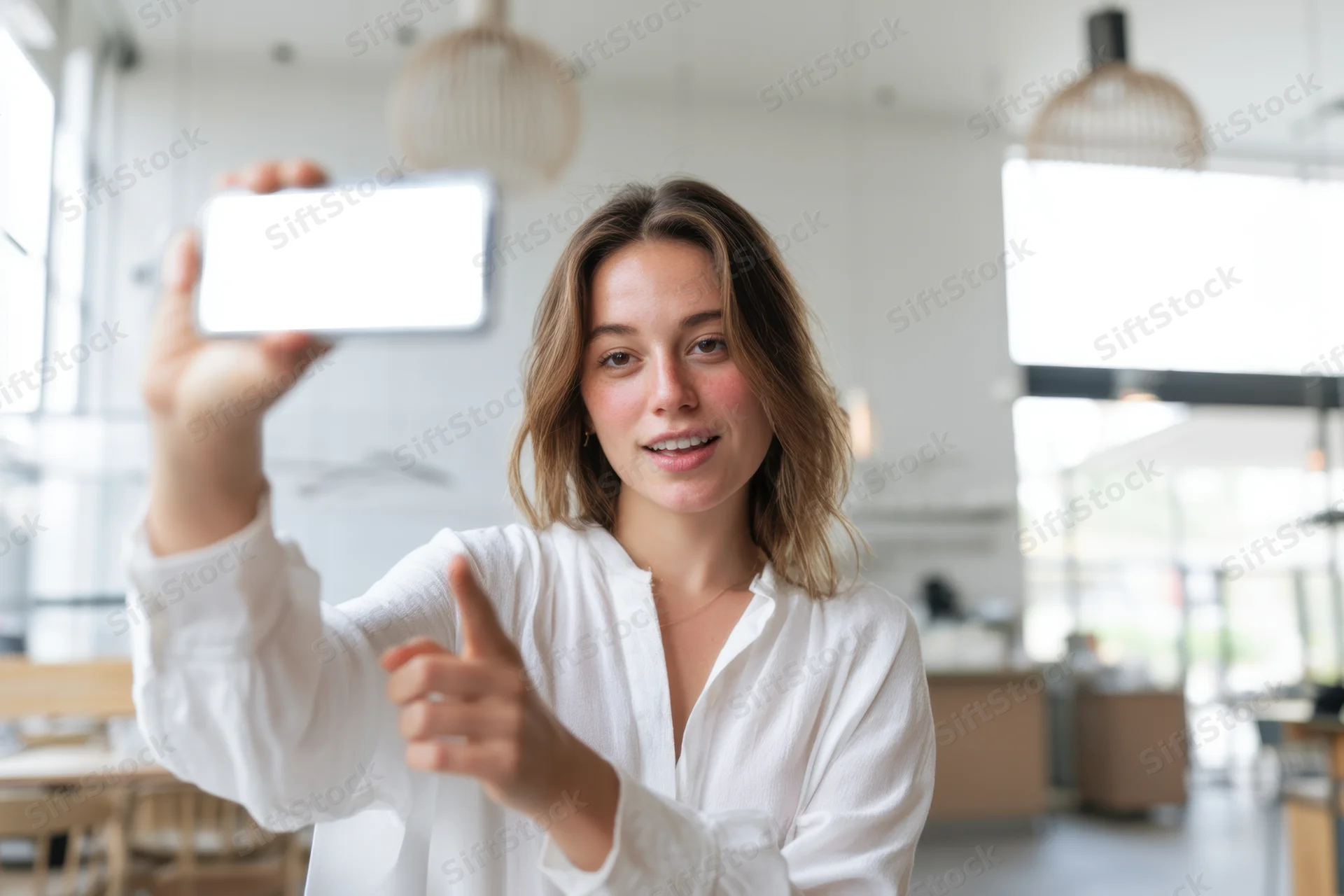 Woman holding smartphone and giving thumbs up in bright modern cafe interior