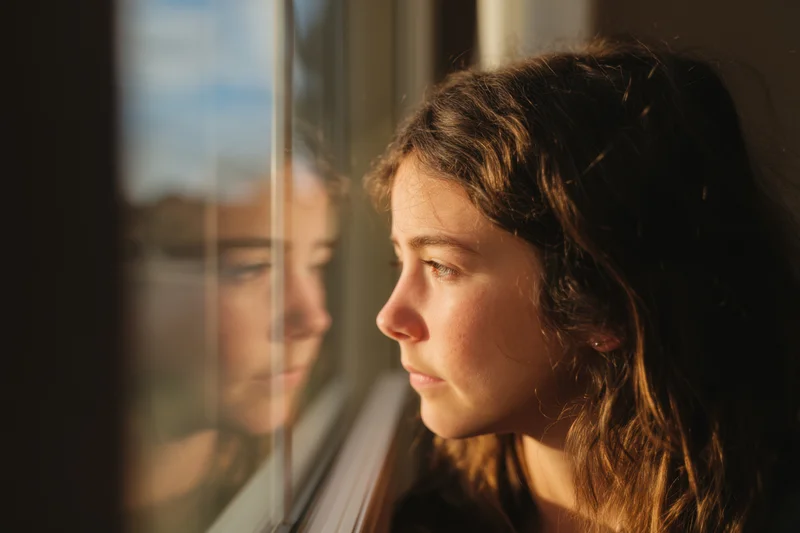 Young girl gazing out of window with reflection visible in glass