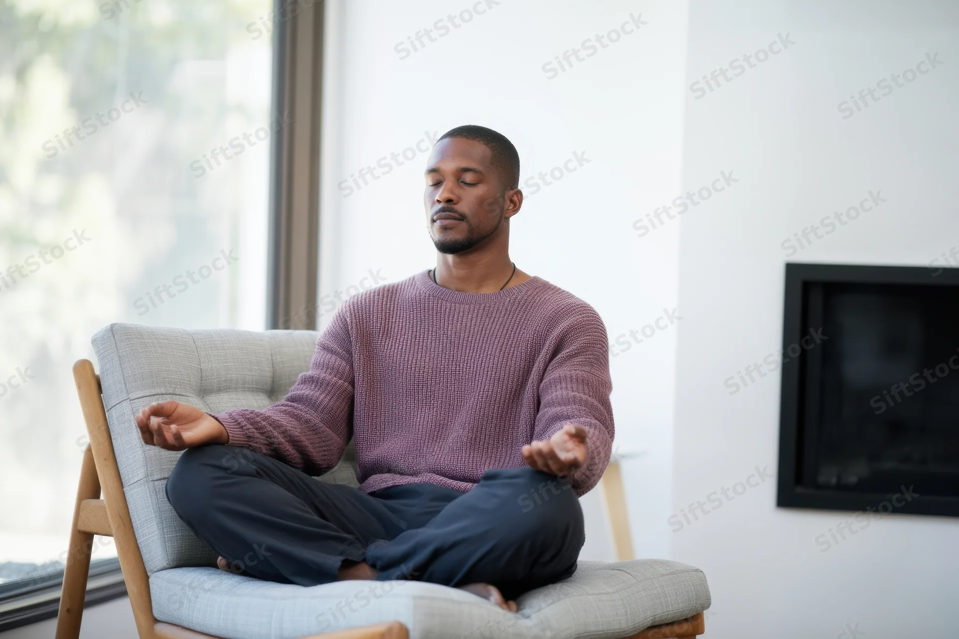 Young man meditating cross-legged on a gray chair in a modern living room