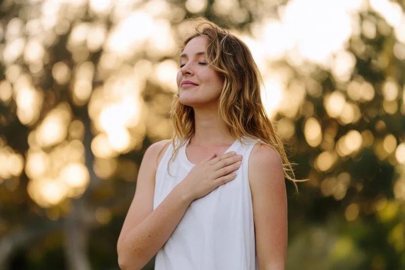 Young woman with eyes closed and hand on chest in a sunlit park