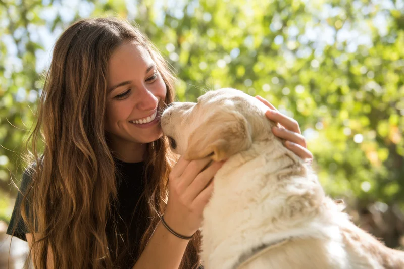 Young woman smiling and hugging a golden retriever outdoors in a sunlit garden