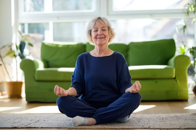 Senior woman meditating cross legged on a rug in a sunlit living room