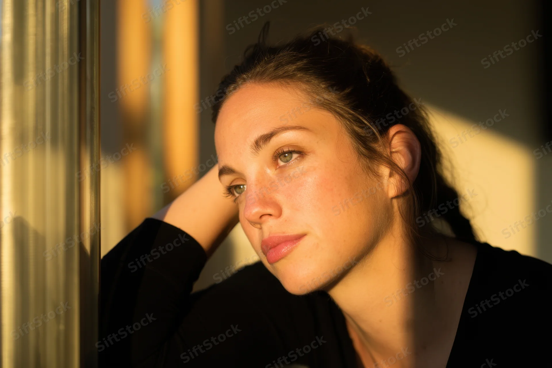 Woman in contemplative side profile by window with warm sunlight on her face