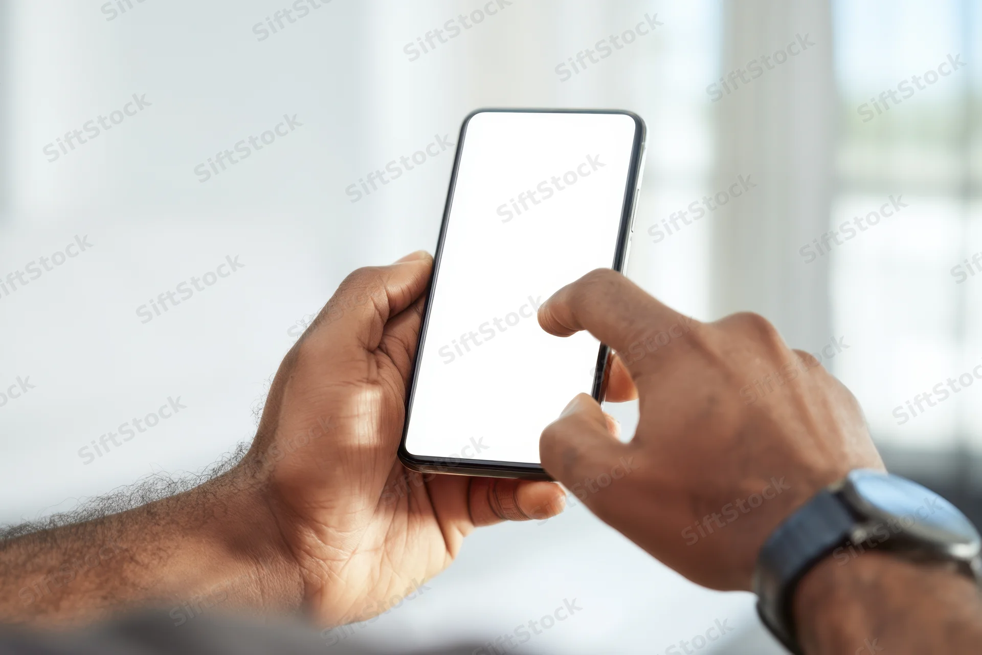Hands holding smartphone with blank white screen, one finger touching display, indoors near window
