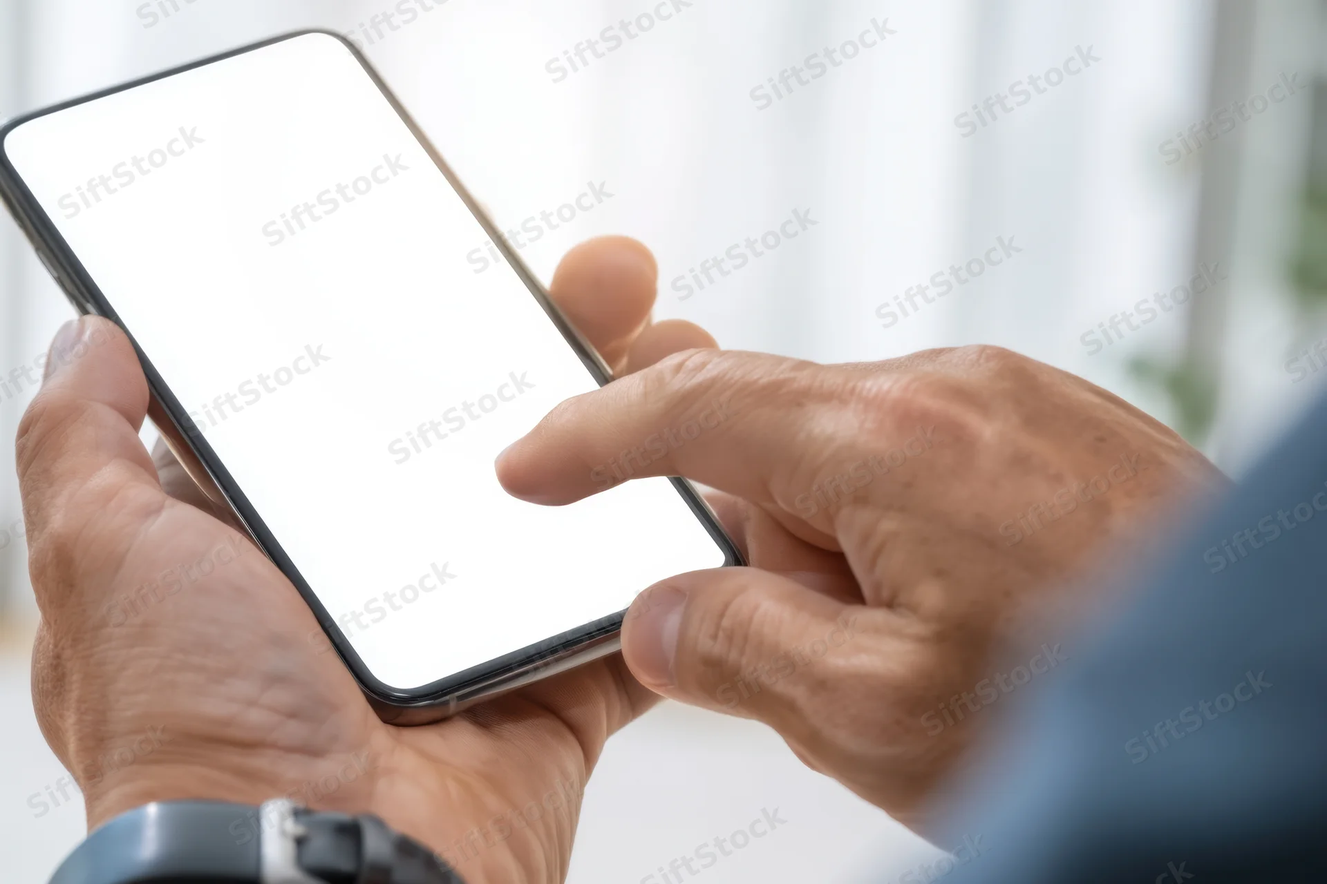 Close-up of hands holding a smartphone with a blank white screen, finger tapping the display indoors