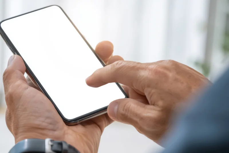 Close-up of hands holding a smartphone with a blank white screen, finger tapping the display indoors