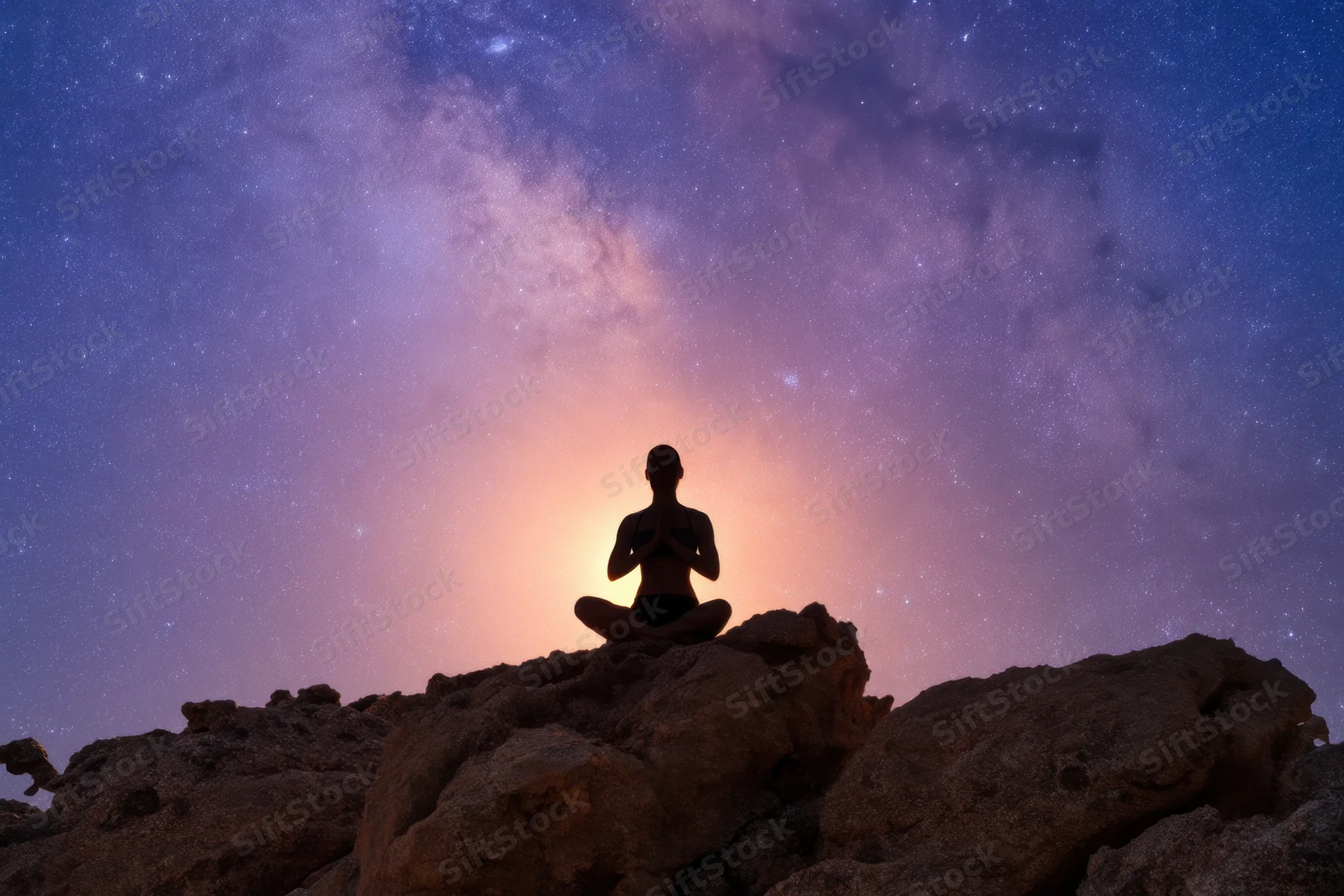 Woman meditating in lotus pose on rocky outcrop under starry night sky